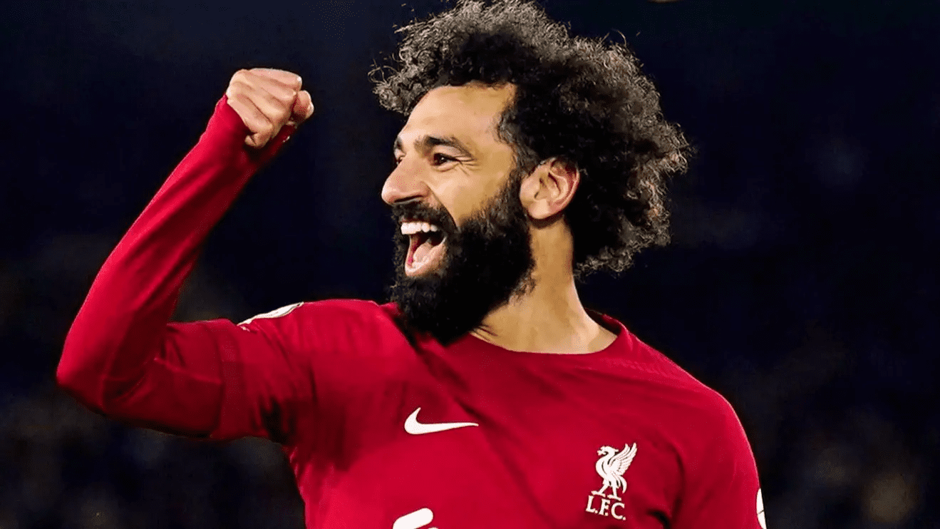 محمد صلاح في الملعب رافع ذراعه وهو يضحك مرتديًا قميص لفربول الأحمر المصدر موقع بوابة الصبح